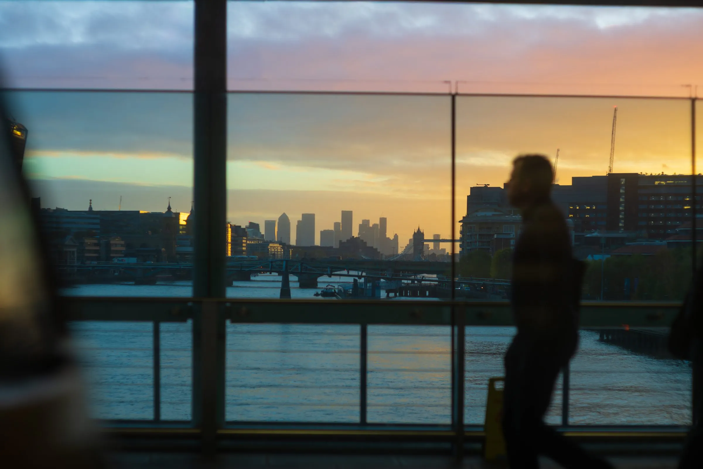 The Thames at sunrise, looking east to Tower Bridge and Canary Wharf, with a commuter walking past